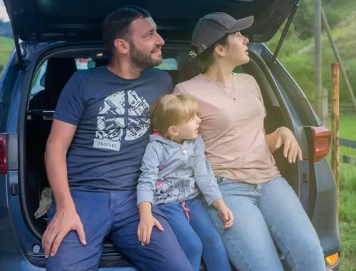 Gezin met een klein kindje zit samen in de open kofferbak van de auto in het groen