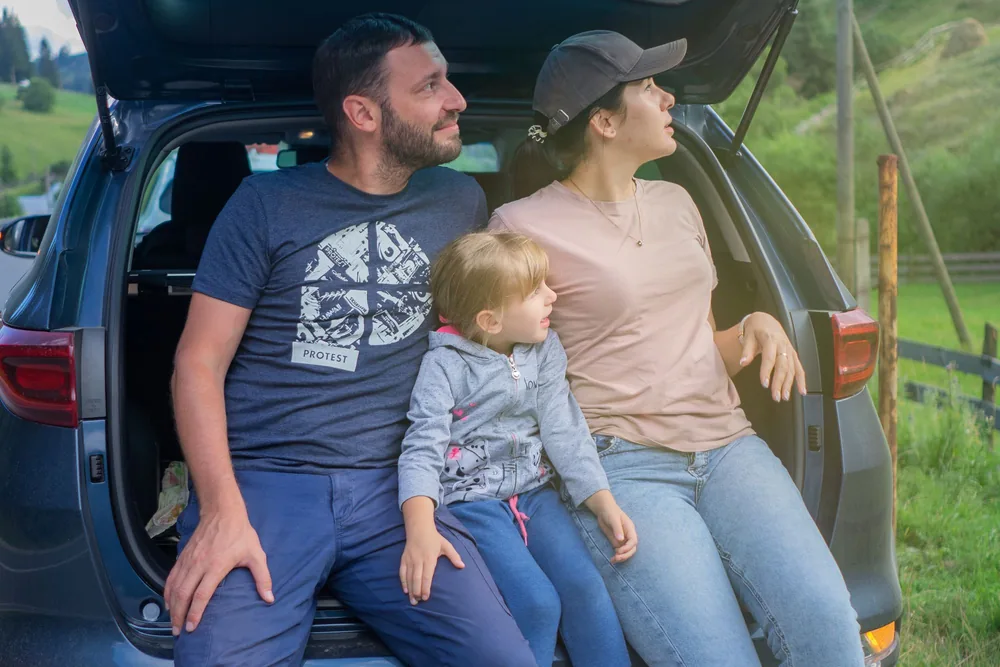 Gezin met een klein kindje zit samen in de open kofferbak van de auto in het groen