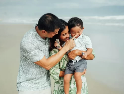 Ouders met hun peuter lachend op het strand tijdens een kindvriendelijke vakantie