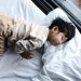 Een jong kind in pyjama slaapt op een groot wit bed bij het raam