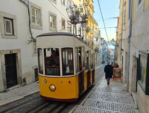 Een geel kabeltreintje in een steil straatje met kasseien in Lissabon