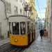 Een geel kabeltreintje in een steil straatje met kasseien in Lissabon