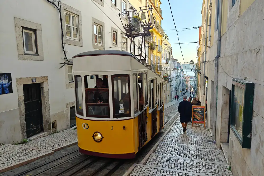 Een geel kabeltreintje in een steil straatje met kasseien in Lissabon
