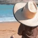 Een peuter met een grote strohoed zit op het strand en kijkt naar de zee