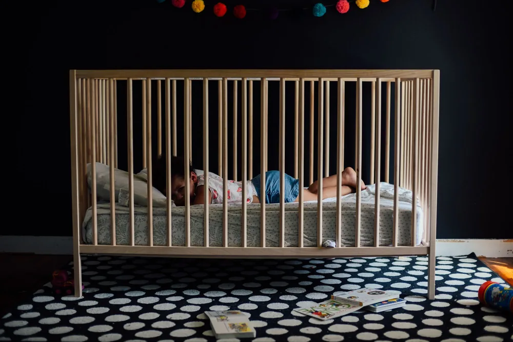 Een peuter slaapt rustig in een houten ledikantje in een donkere kamer
