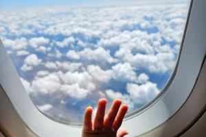 Een kinderhandje tegen het raam van een vliegtuig boven de wolken
