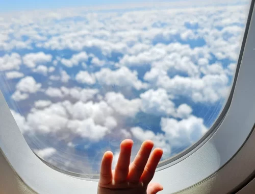 Een kinderhandje tegen het raam van een vliegtuig boven de wolken