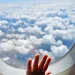 Een kinderhandje tegen het raam van een vliegtuig boven de wolken