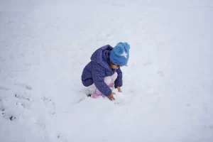 Een peuter in een warme winterjas en muts speelt gehurkt in de verse sneeuw