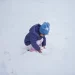 Een peuter in een warme winterjas en muts speelt gehurkt in de verse sneeuw