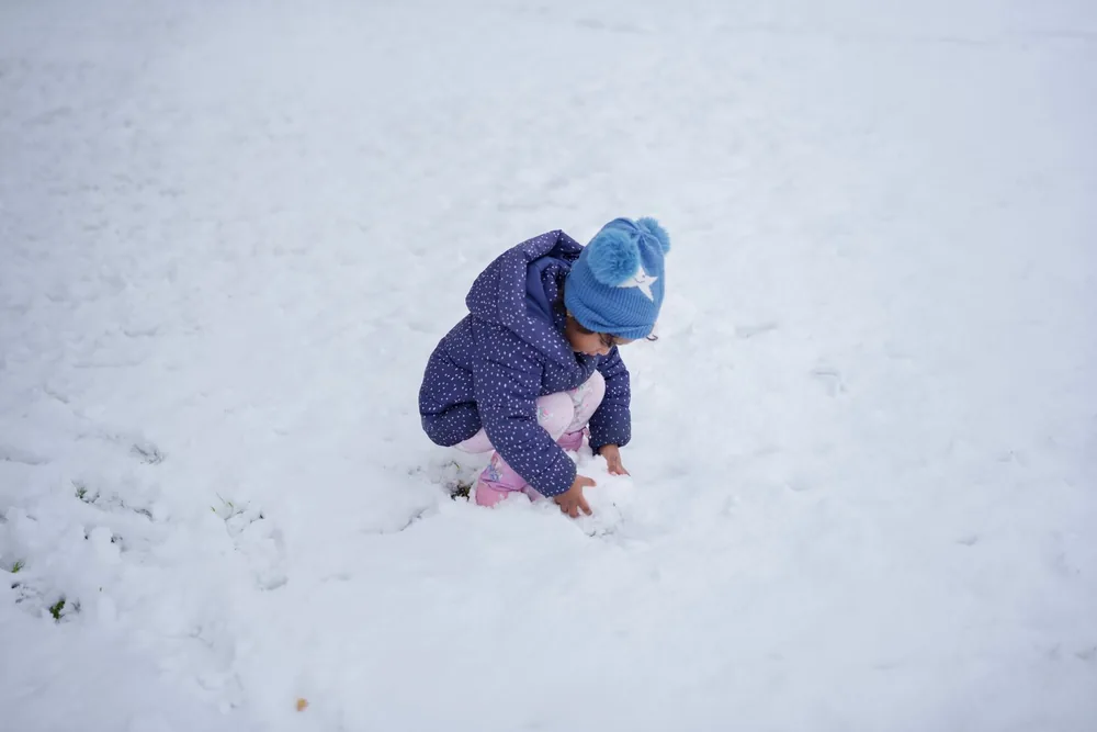 Een peuter in een warme winterjas en muts speelt gehurkt in de verse sneeuw